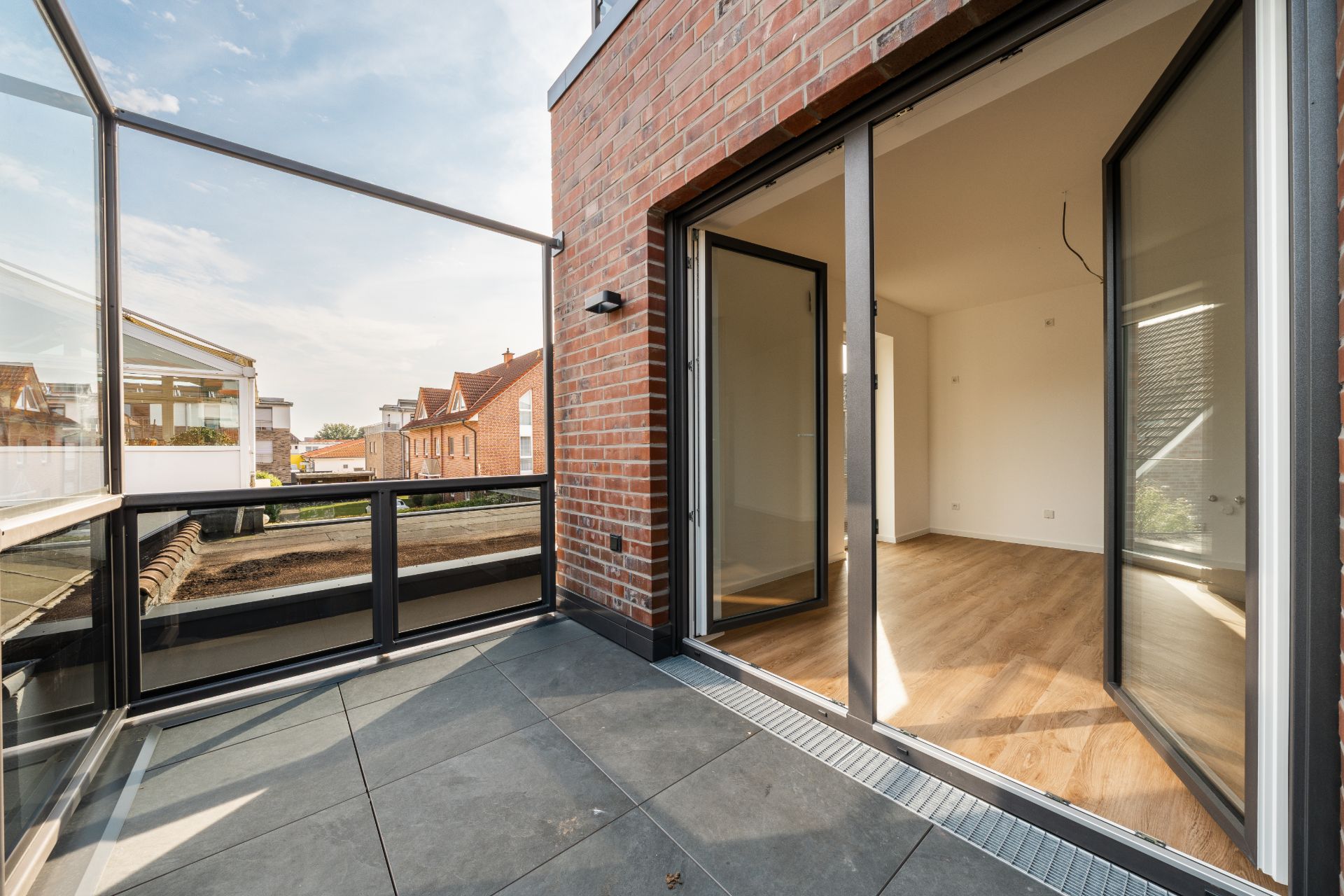 Moderner Balkon mit Glasgeländer und Zugang zu einem hellen Zimmer mit Holzboden.