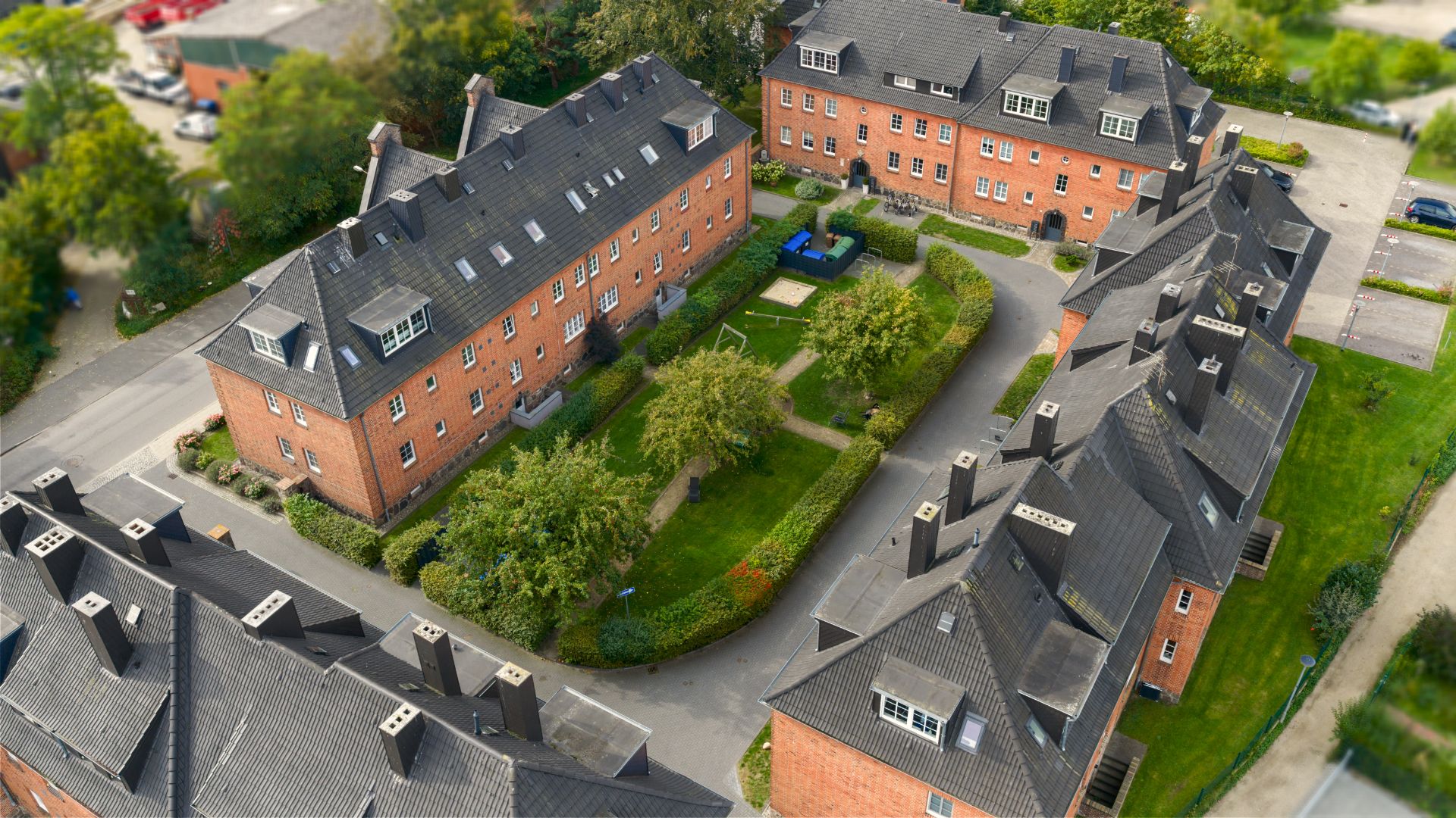 Luftaufnahme mehrerer roter Wohnhäuser mit Innenhof und grüner Gartenanlage.