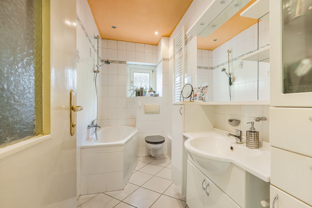 Helles Badezimmer mit Badewanne, Waschbecken, Spiegel, WC und weißer Fliesenwand.