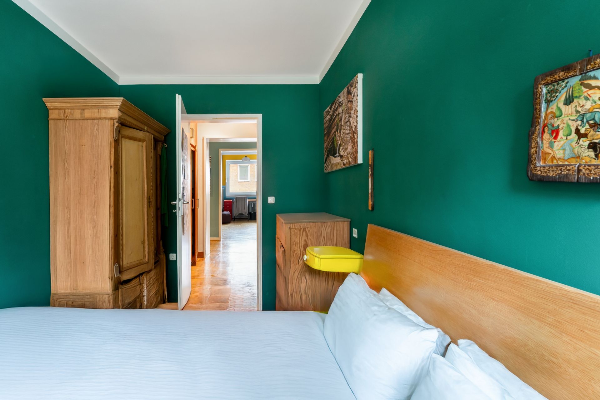 Schlafzimmer mit grün gestrichenen Wänden, Holzbett, Schrank und offener Tür zum Flur.