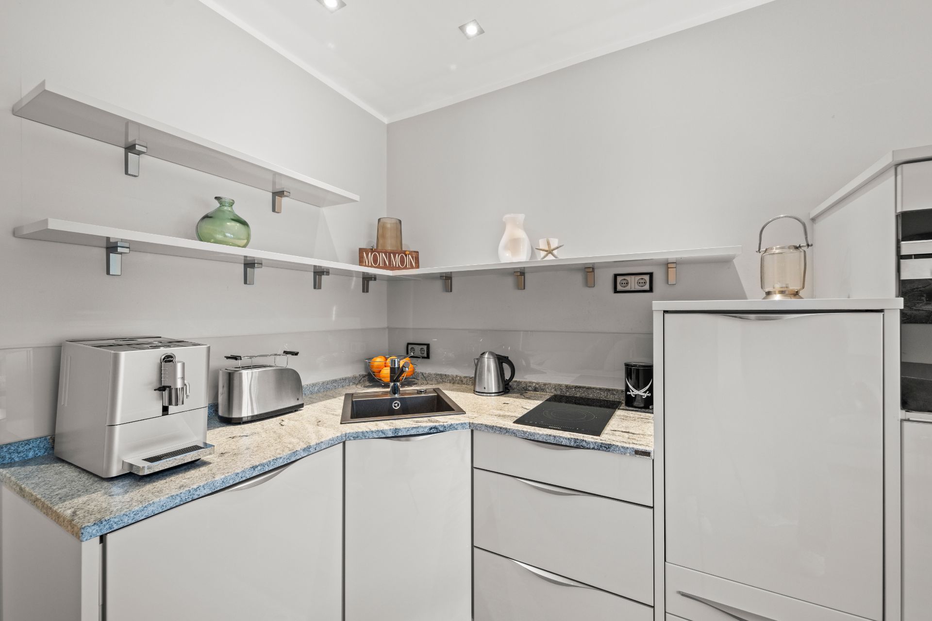 Moderne, helle Küche mit Kaffeemaschine, Toaster, Herdplatte, Spüle und offenen Regalen.