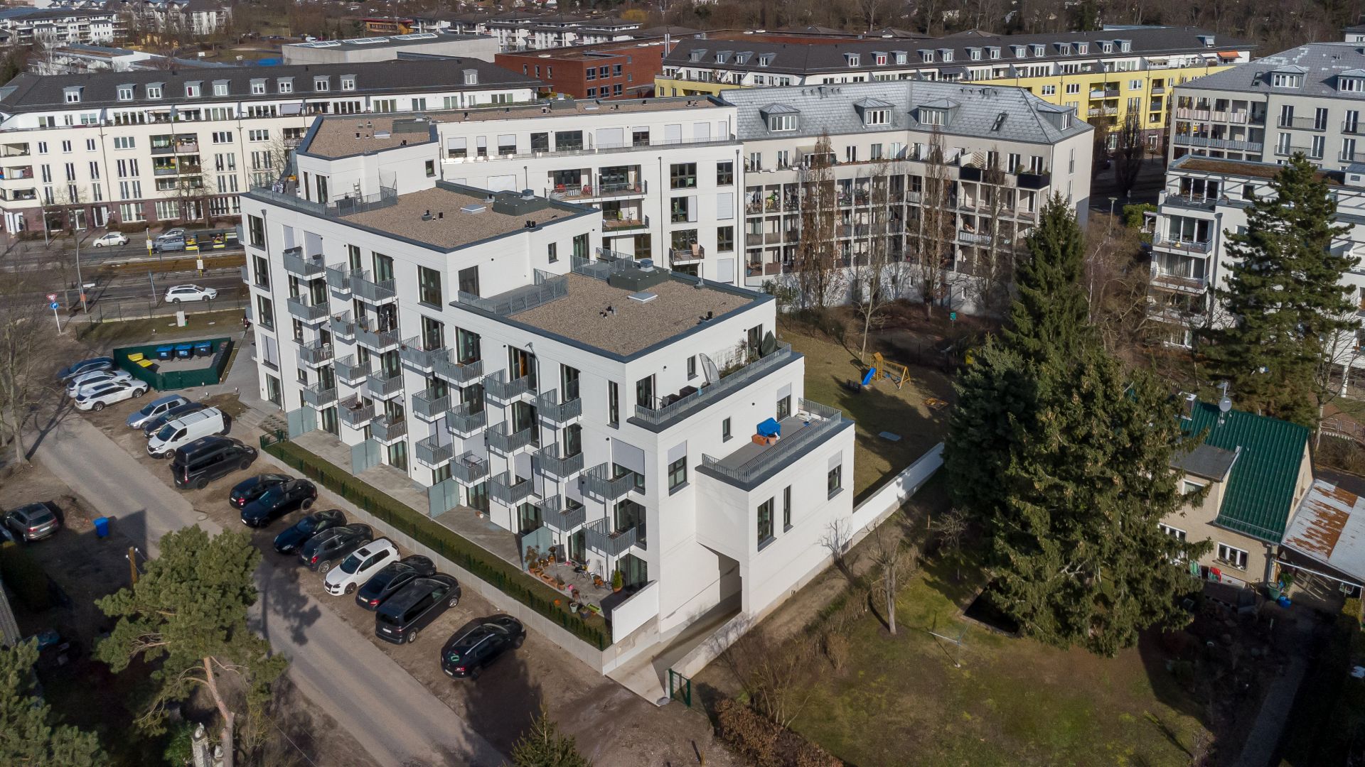 Mehrstöckiges Wohngebäude mit Balkonen und parkenden Autos davor, umgeben von weiteren Wohnhäusern.