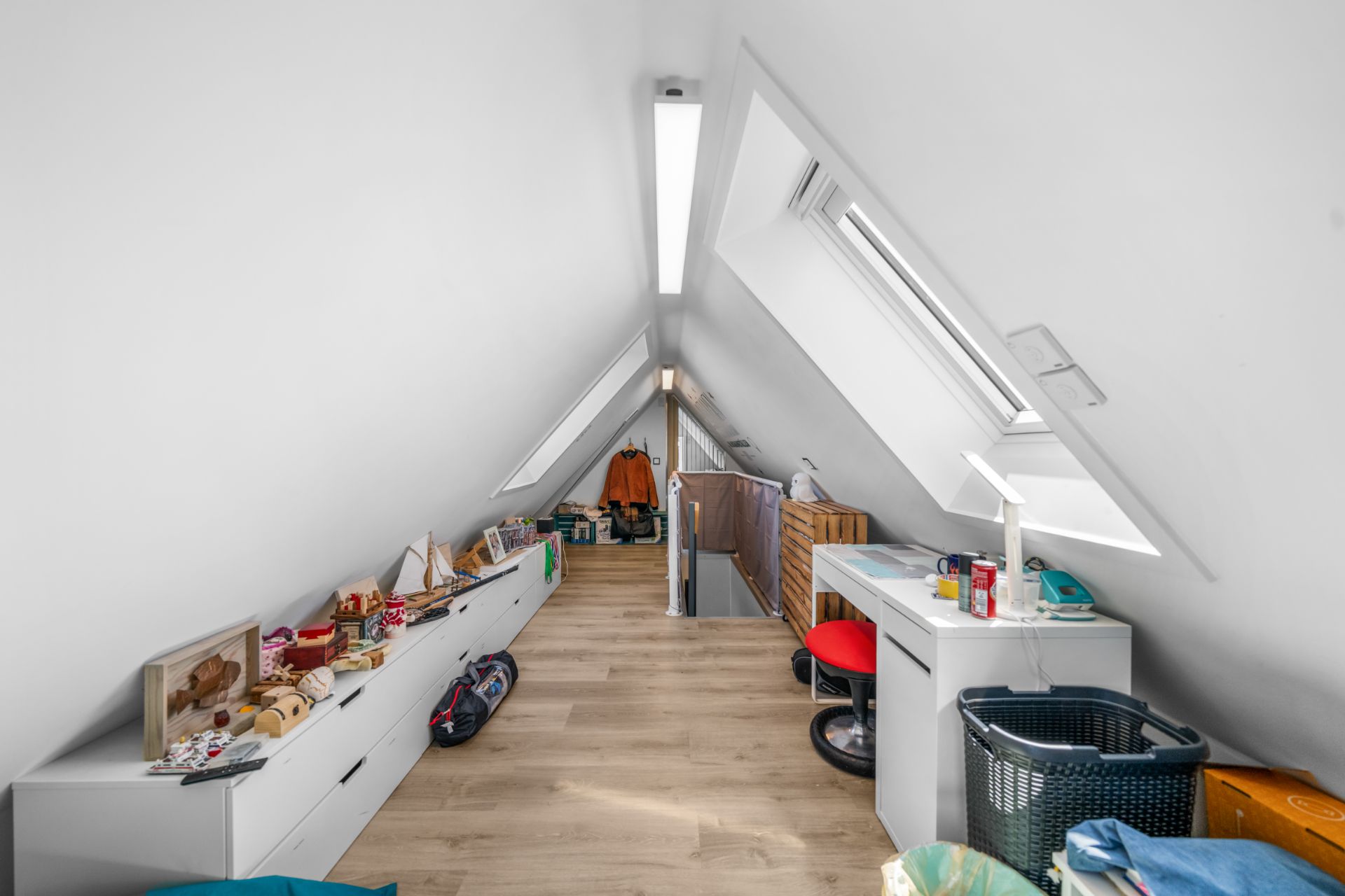Heller Dachboden mit Schreibtisch, Spielzeug und Dachfenstern, Holzboden und Stauraum.