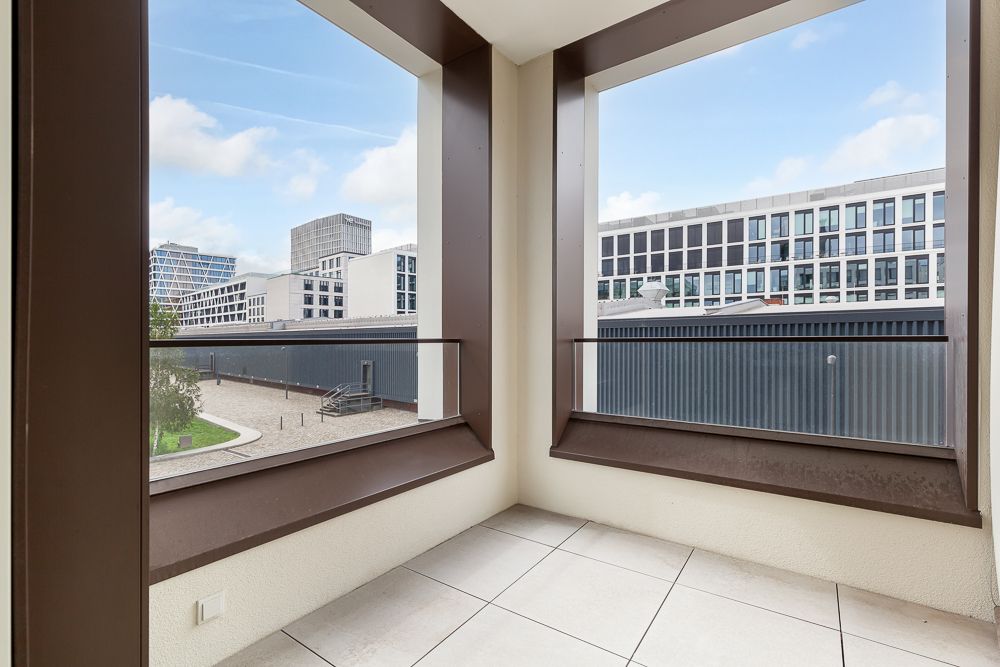 Balkon mit Blick auf einen Innenhof und moderne Bürogebäude im Hintergrund.