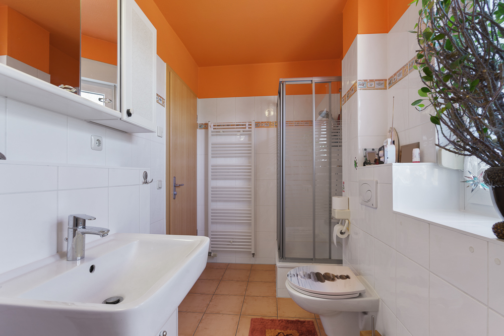 Modernes Badezimmer mit weißer Keramik, Dusche, WC, Waschbecken und orangefarbener Decke.
