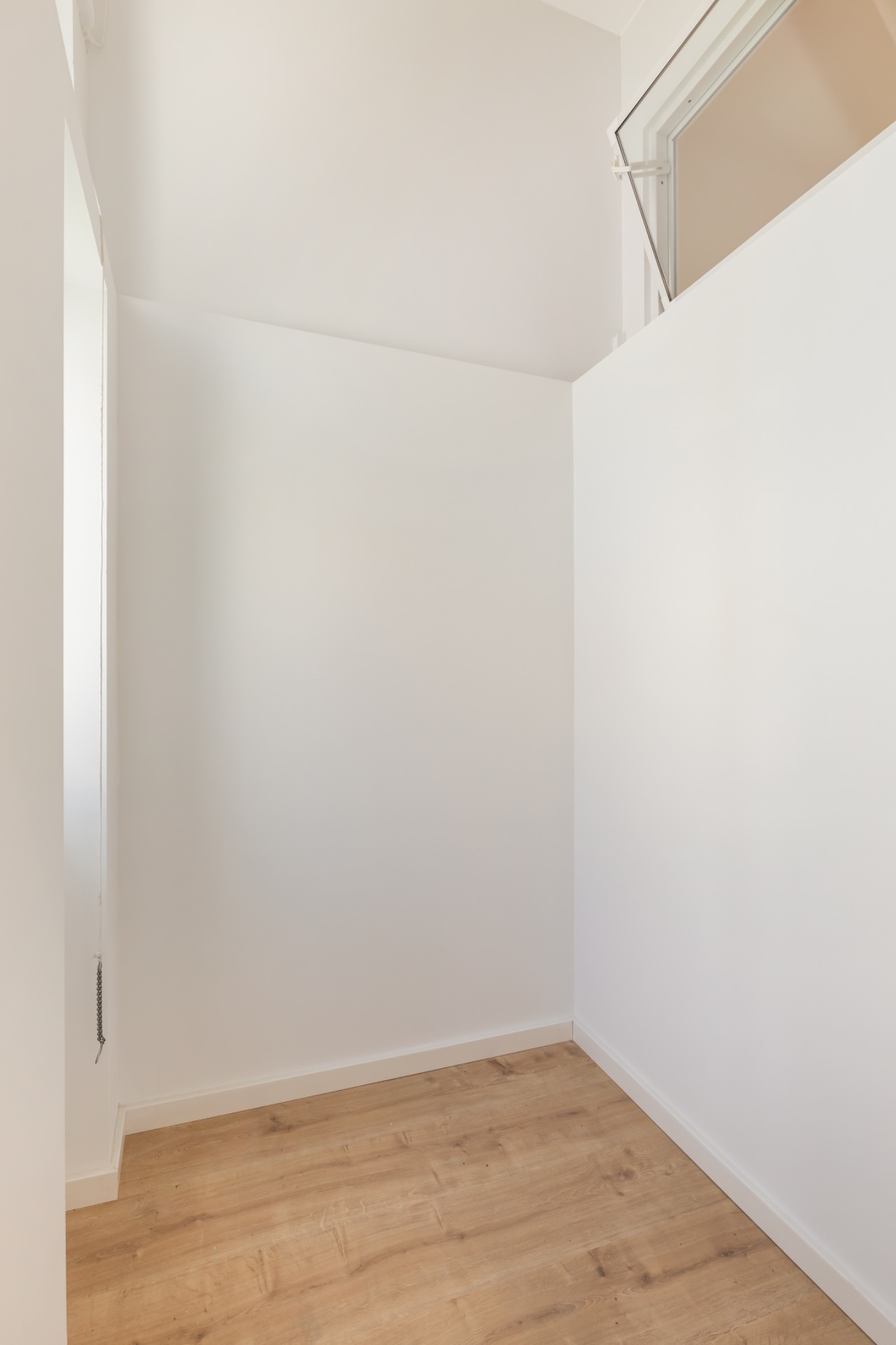 Kleiner, leerer Raum mit weiß gestrichenen Wänden und Holzfußboden.