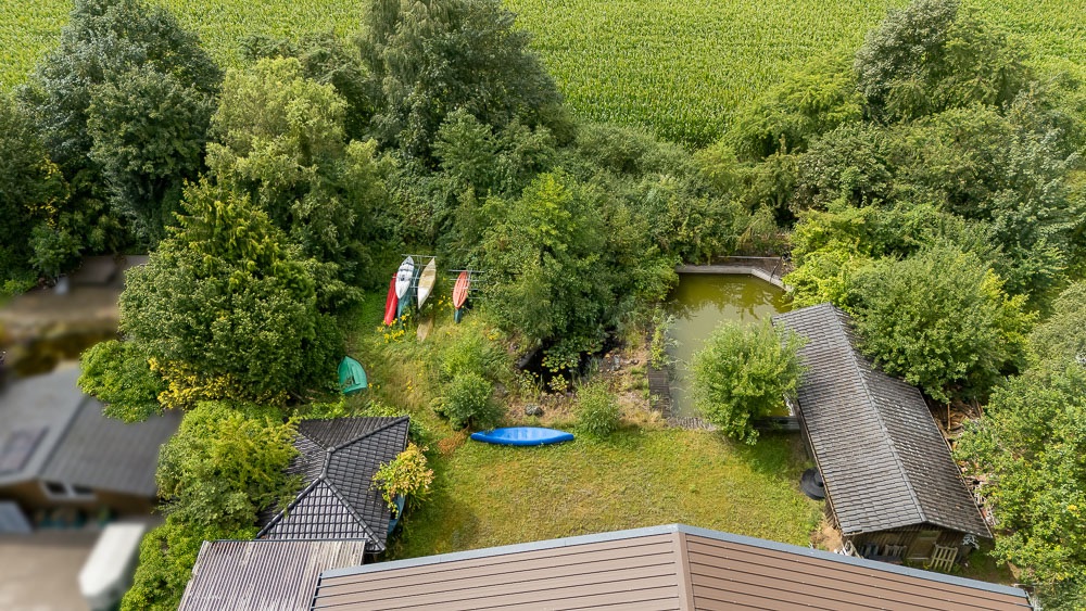 Luftaufnahme eines Gartens mit Teich, Booten, Rasenfläche und zwei Nebengebäuden.