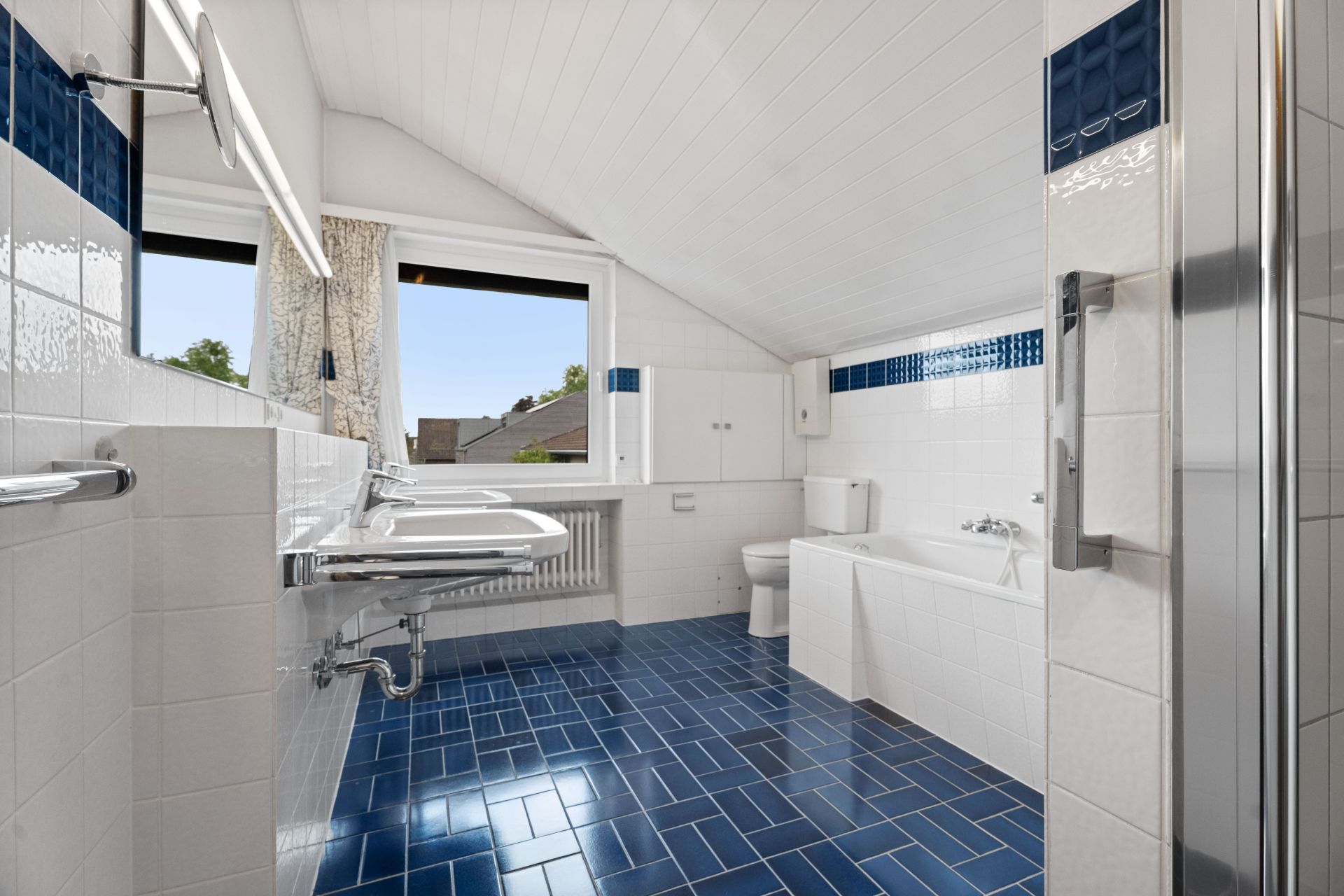 Modernes Badezimmer mit blauen Fliesen, zwei Waschbecken, Badewanne und Fenster.