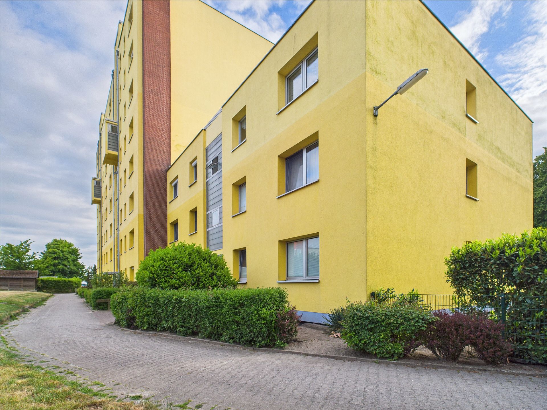 Mehrstöckiges gelbes Wohnhaus mit mehreren Fenstern und umgebenden Büschen.
