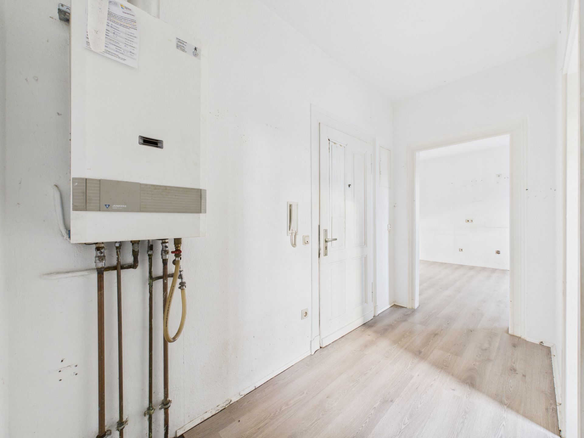 Heller Flur mit weißer Wand, Gastherme und Holzboden in einer Wohnung.