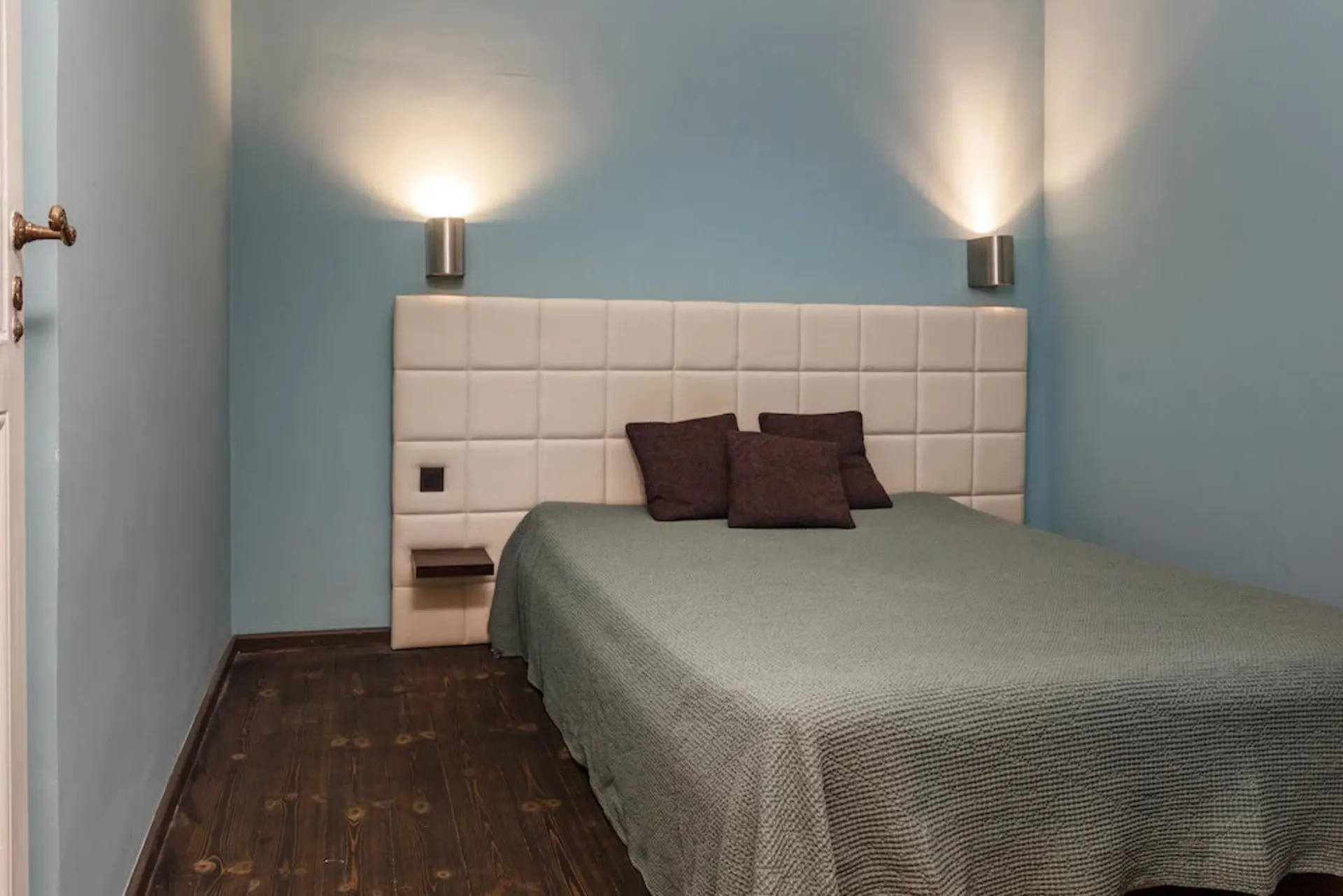 Schlafzimmer mit Bett, gepolstertem Kopfteil, blauer Wand und zwei Wandlampen.
