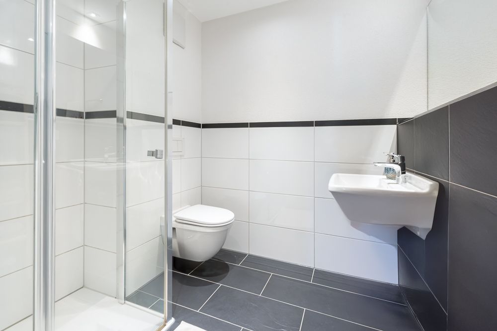 Modernes Badezimmer mit Dusche, Wandtoilette und Waschbecken, weiße und dunkle Fliesen.