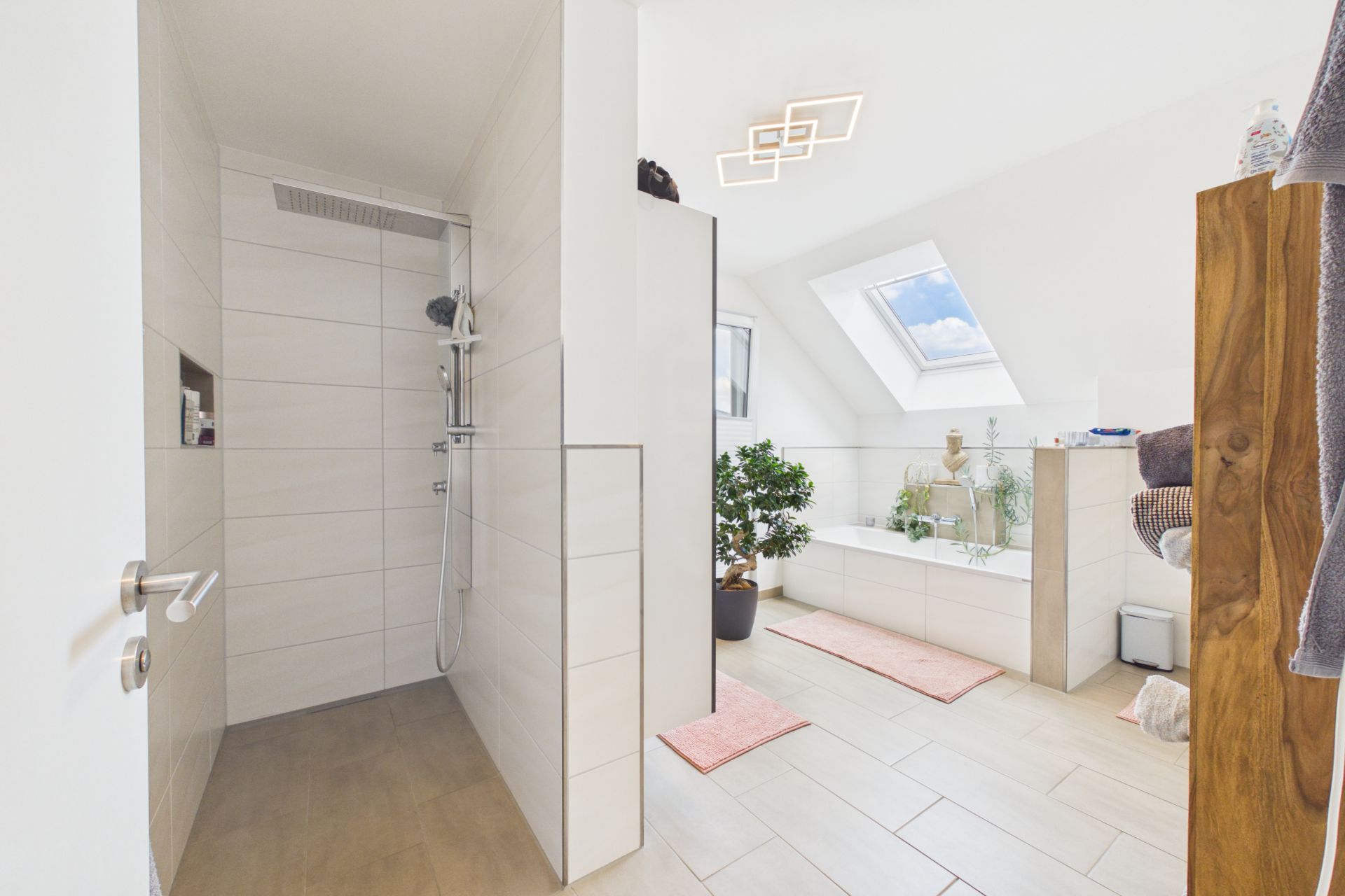 Modernes Badezimmer mit begehbarer Dusche, Badewanne, Dachfenster und Pflanzen.