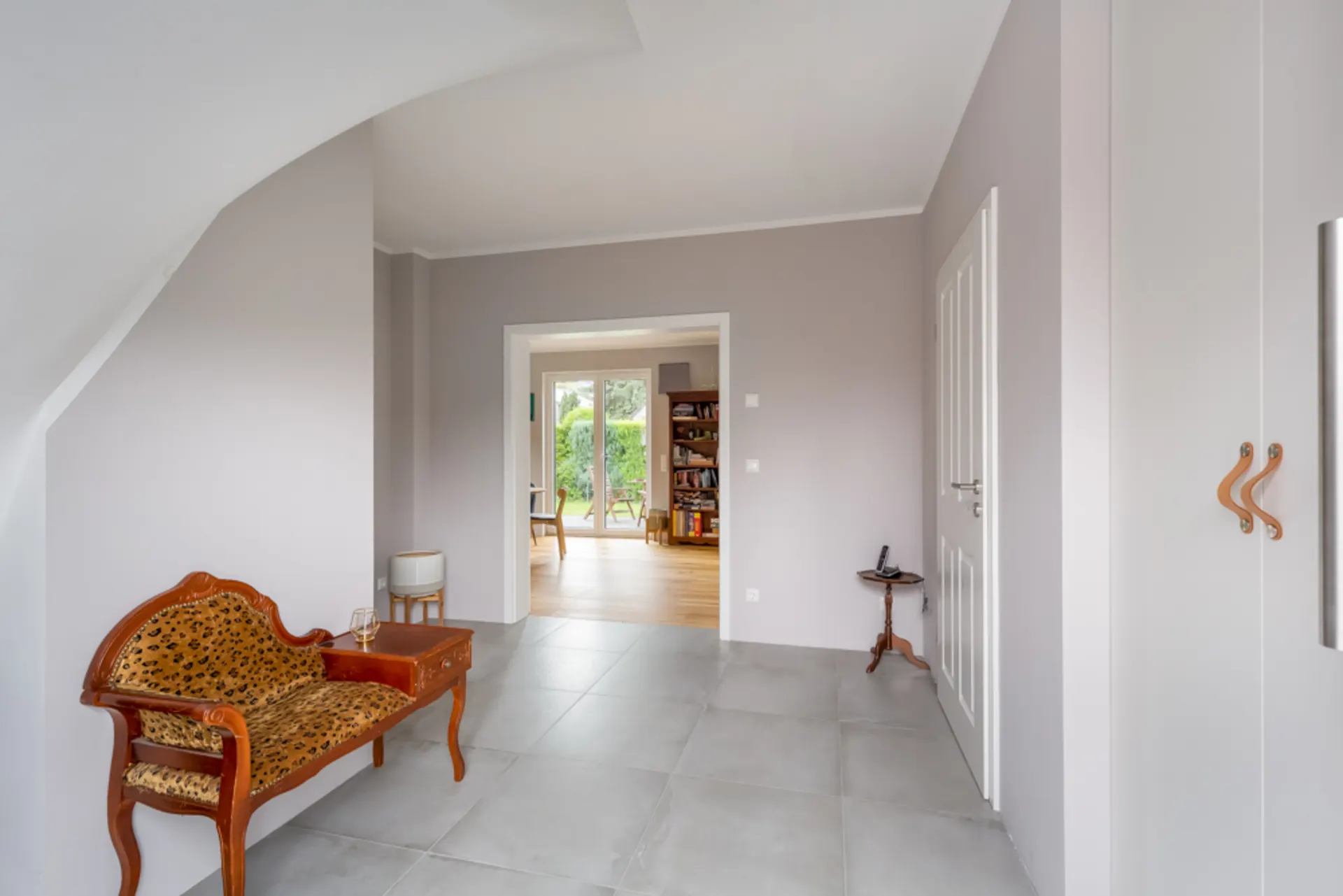 Heller Flur mit Sitzbank, kleinem Tisch, offener Tür zu Wohnzimmer und Blick ins Regal.