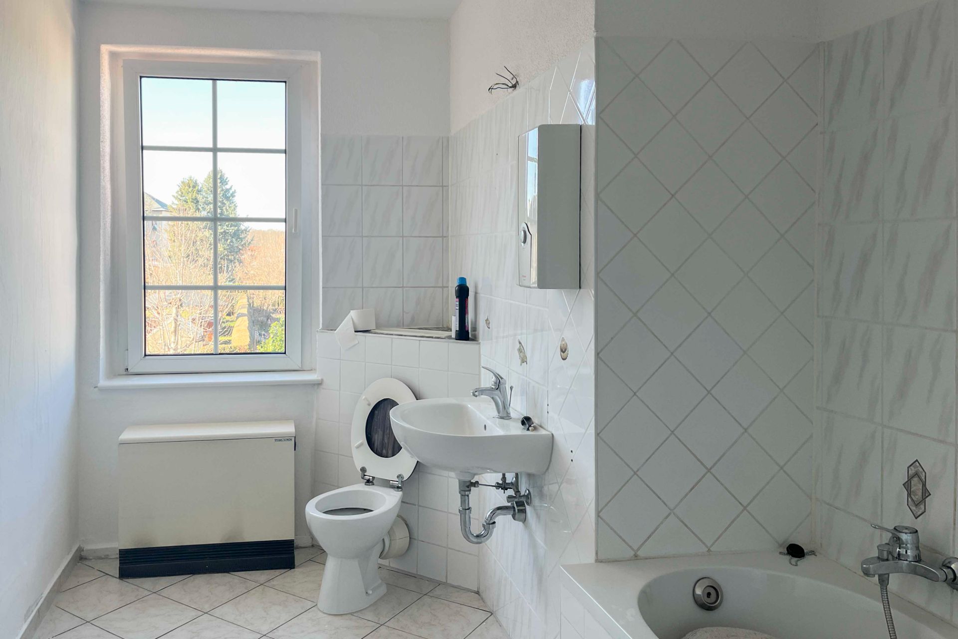 Helles Badezimmer mit Fenster, Toilette, Waschbecken und Badewanne mit weißen Fliesen.