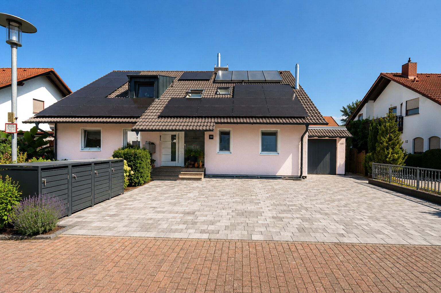 Modernes Einfamilienhaus mit Solarpanels auf dem Dach und großem gepflastertem Vorhof.