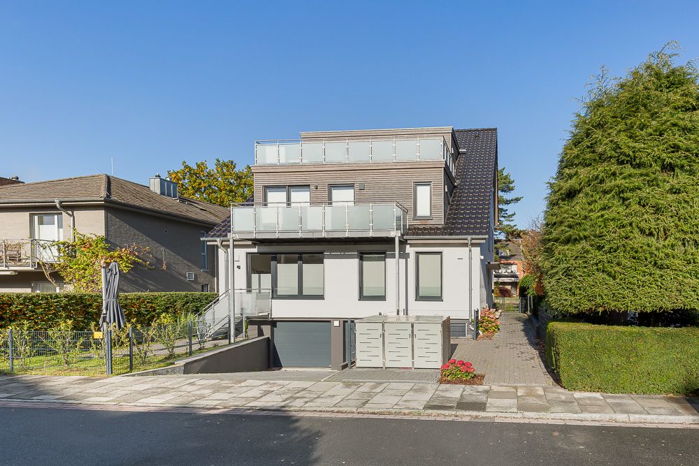 Modernes Wohnhaus mit Balkon, Einfahrt zur Garage und Vorgarten, tagsüber aufgenommen.