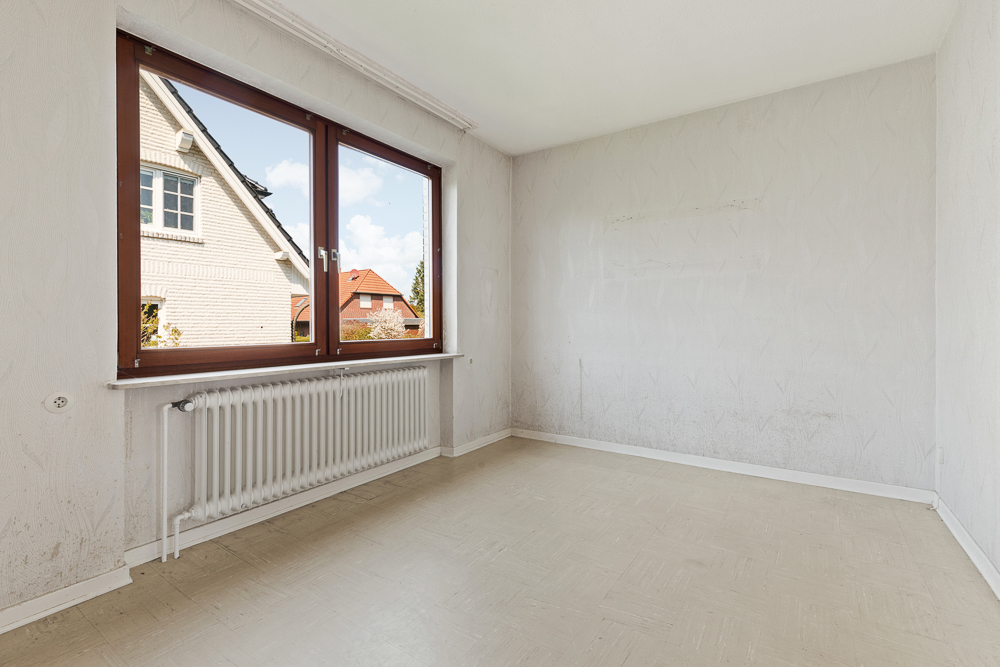 Leerer Raum mit großem Fenster, weißer Heizung und Blick auf Nachbarhäuser.