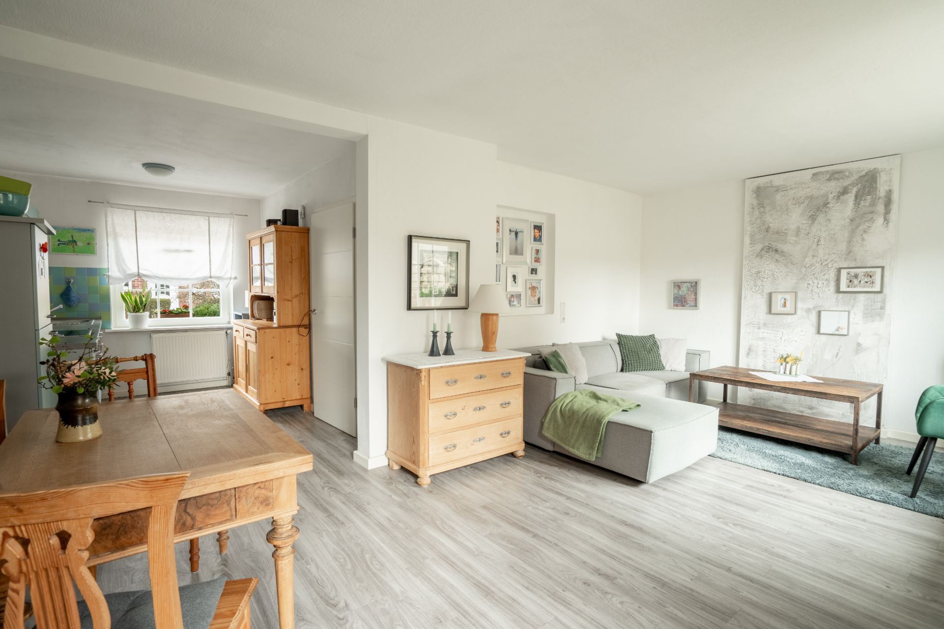 Helles Wohnzimmer mit Sofa, Couchtisch, Esstisch und Holzmöbeln auf Laminatboden.