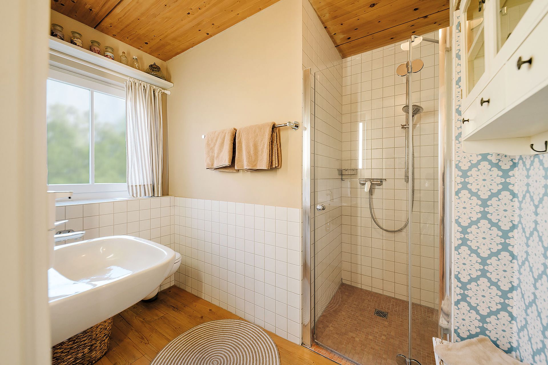 Helles Badezimmer mit Dusche, Badewanne, Fenster und zwei beigen Handtüchern an der Wand.