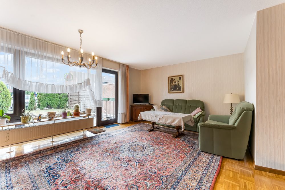 Helles Wohnzimmer mit grünem Sofa, großem Teppich, Kronleuchter und bodentiefen Fenstern.