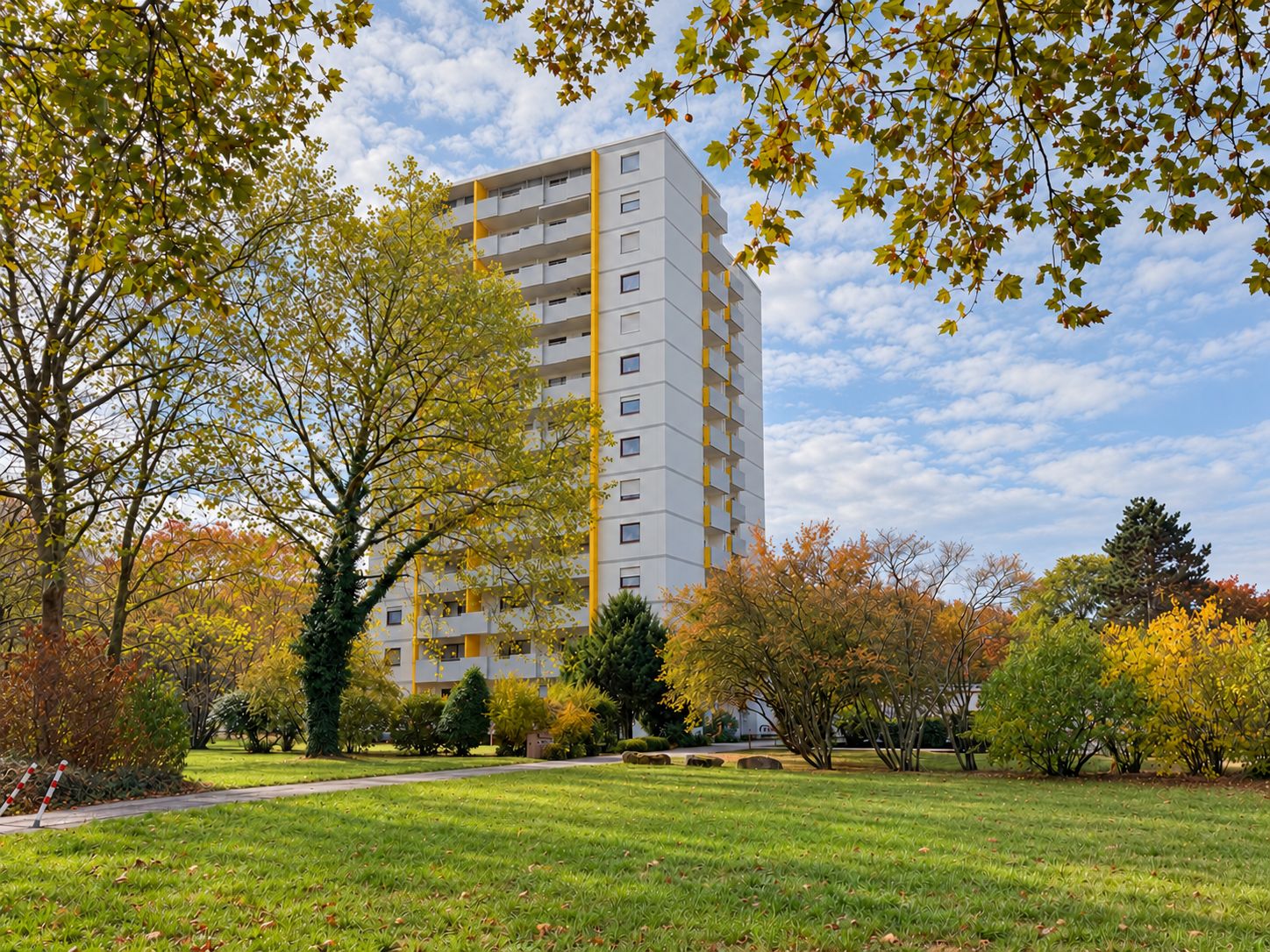 Wohnhaus mit mehreren Stockwerken, umgeben von Bäumen und einer großen Wiese.