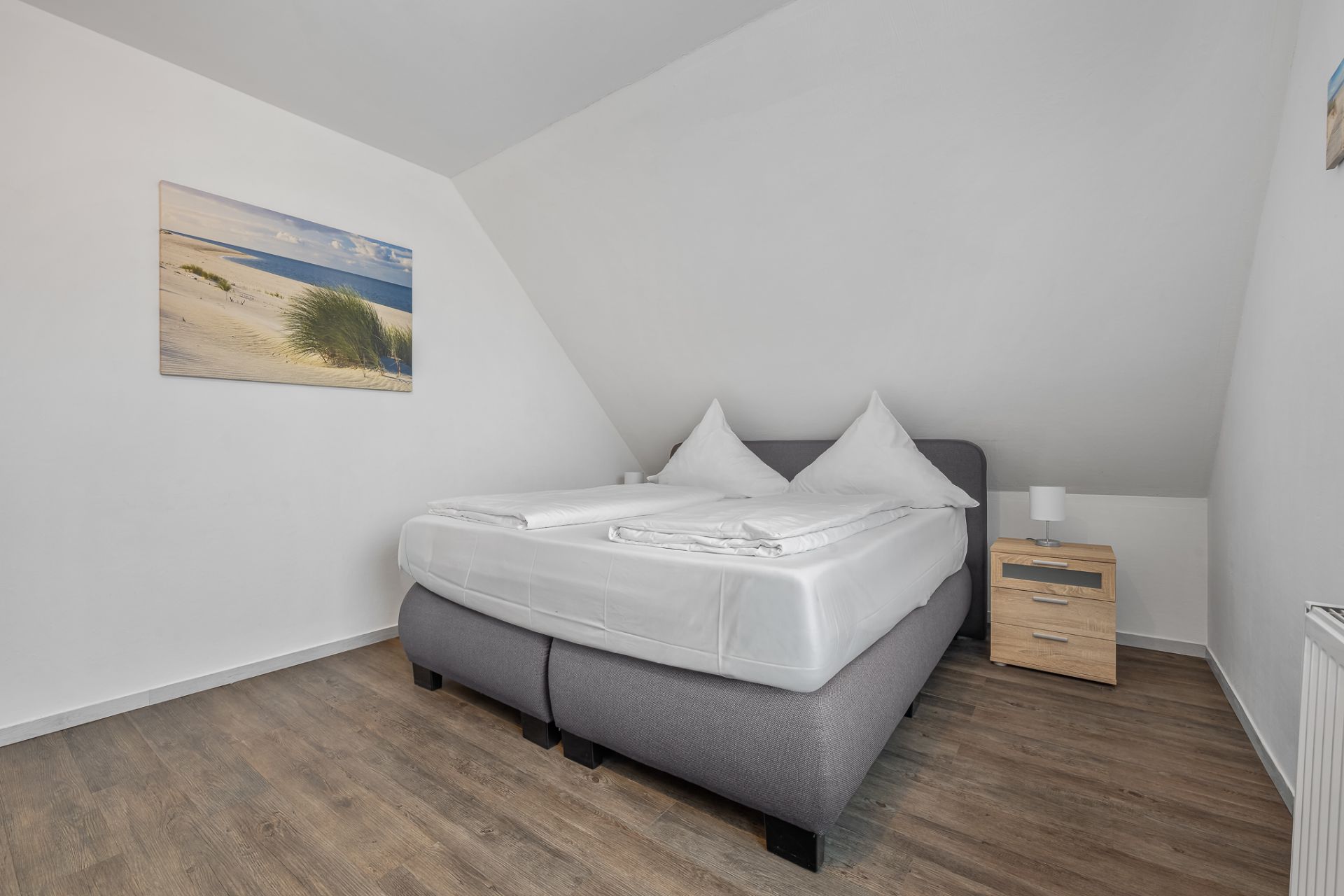 Schlafzimmer mit Doppelbett, Nachttisch und Bild an der Wand.