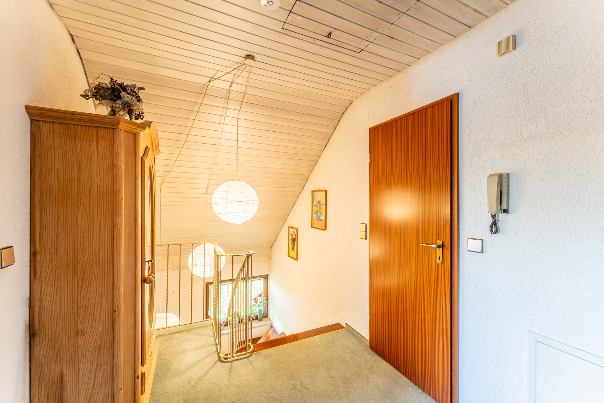 Heller Flur mit Holzschrank, Treppe, Holztür, Bildern an der Wand und runden Deckenlampen.