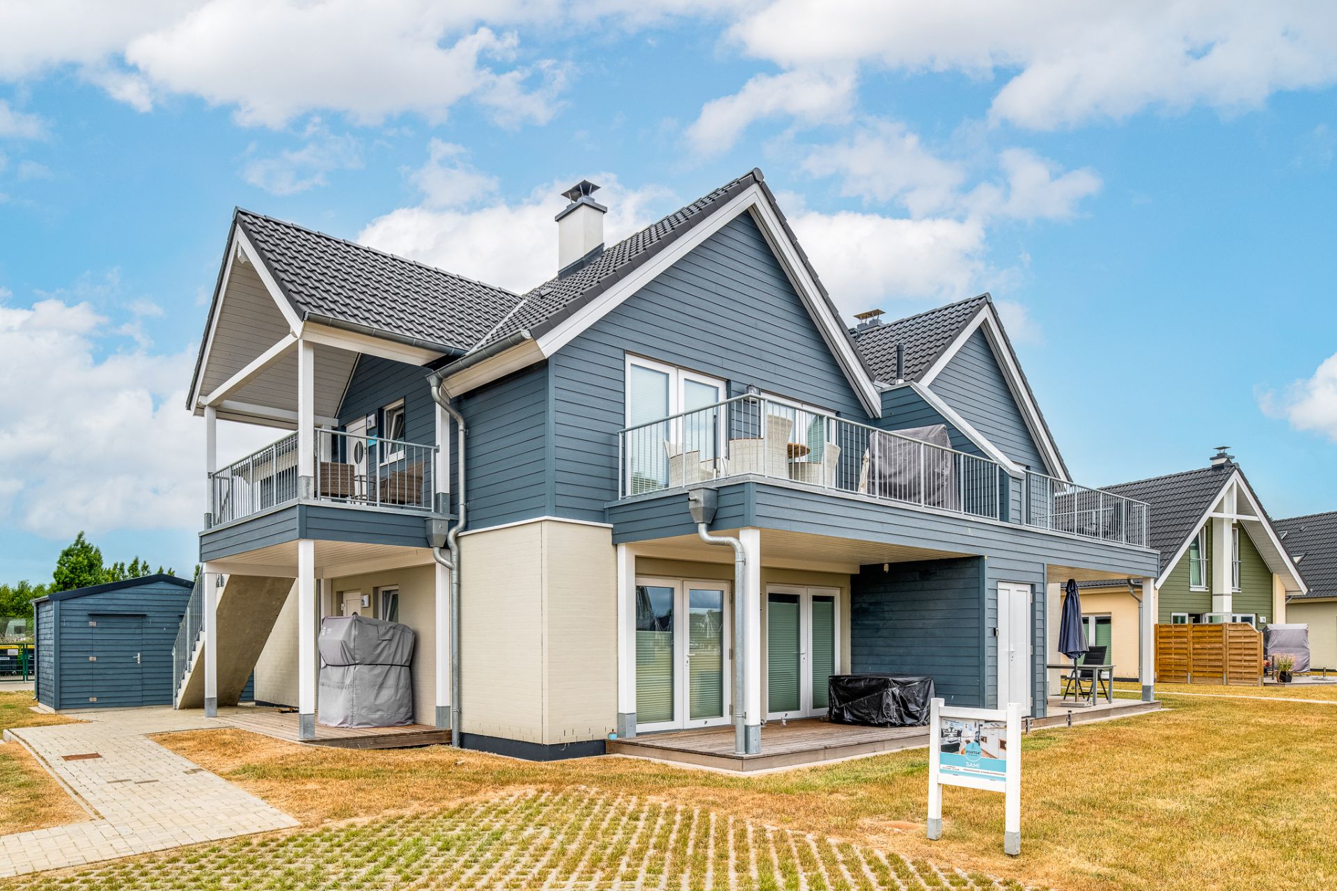 Modernes Einfamilienhaus mit Balkon und Terrasse auf einer Rasenfläche bei Tageslicht.
