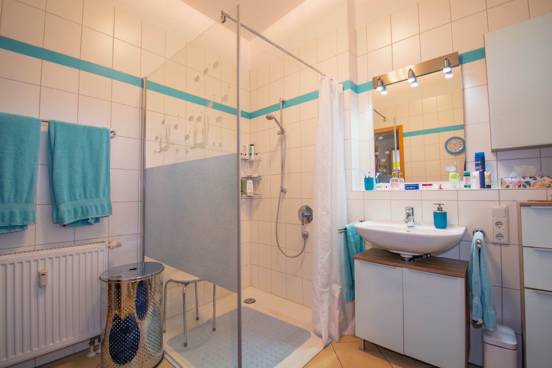 Modernes Badezimmer mit Dusche, Waschbecken, Spiegel und blauen Handtüchern.