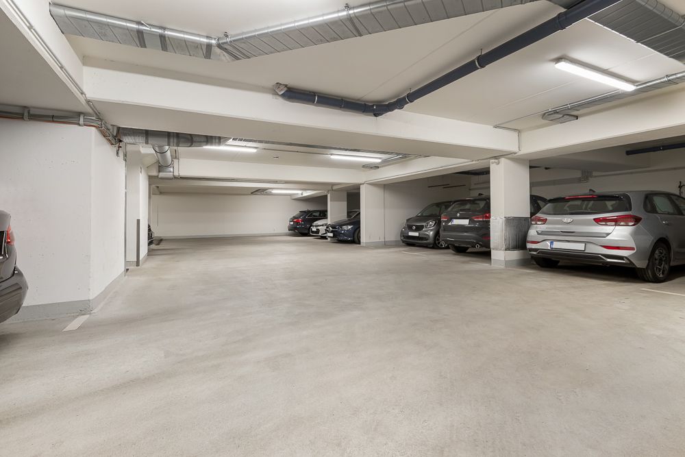 Helle Tiefgarage mit mehreren geparkten Autos und freien Stellplätzen.