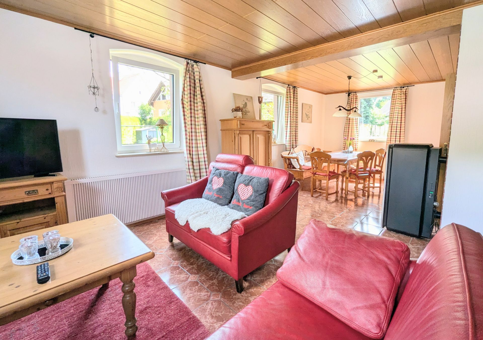 Helles Wohnzimmer mit roten Sofas, TV, Holztisch und angrenzendem Essbereich mit Holztisch und Stühlen.
