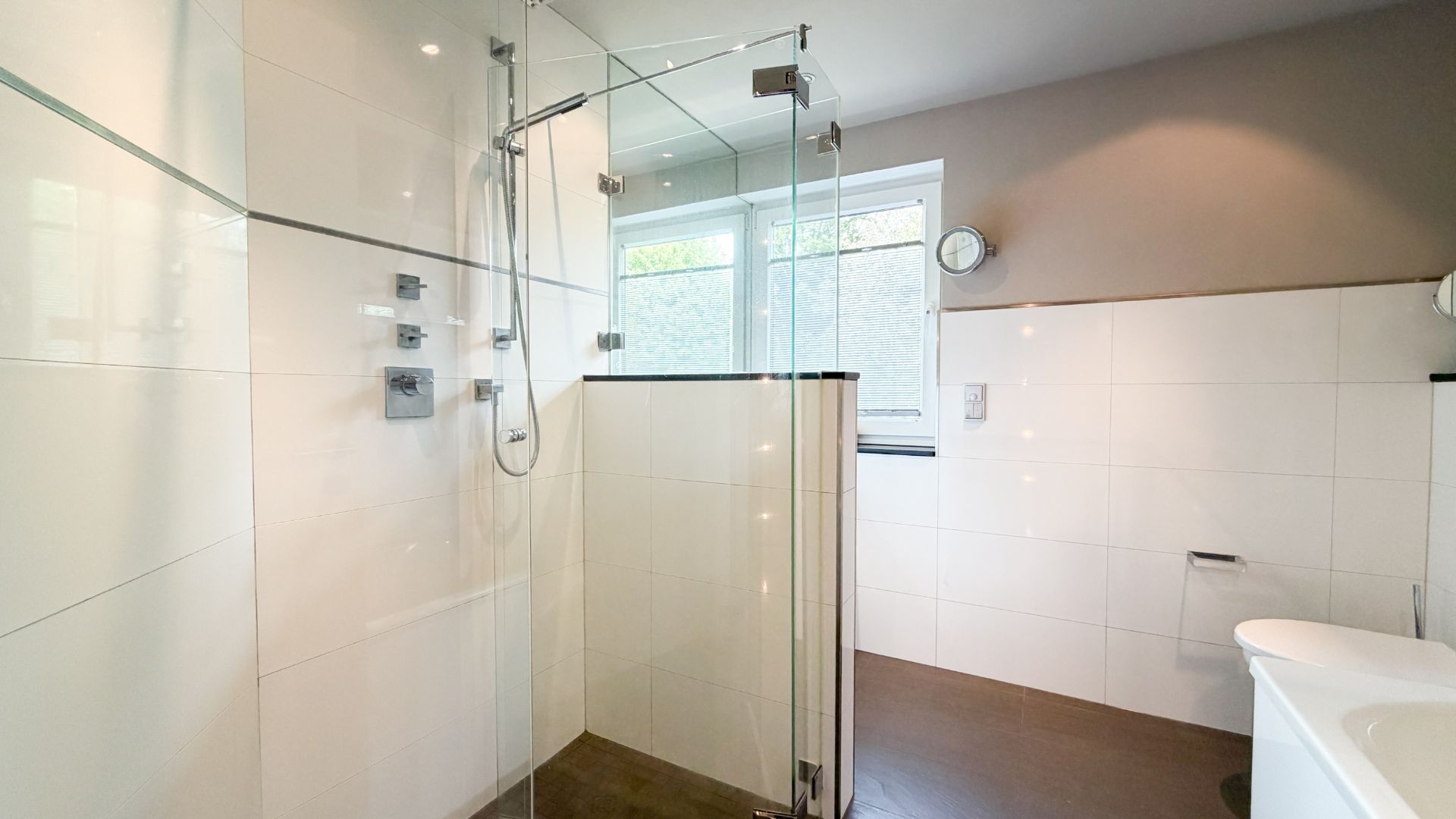 Modernes Badezimmer mit begehbarer Dusche, Fenster und weiß gefliesten Wänden.