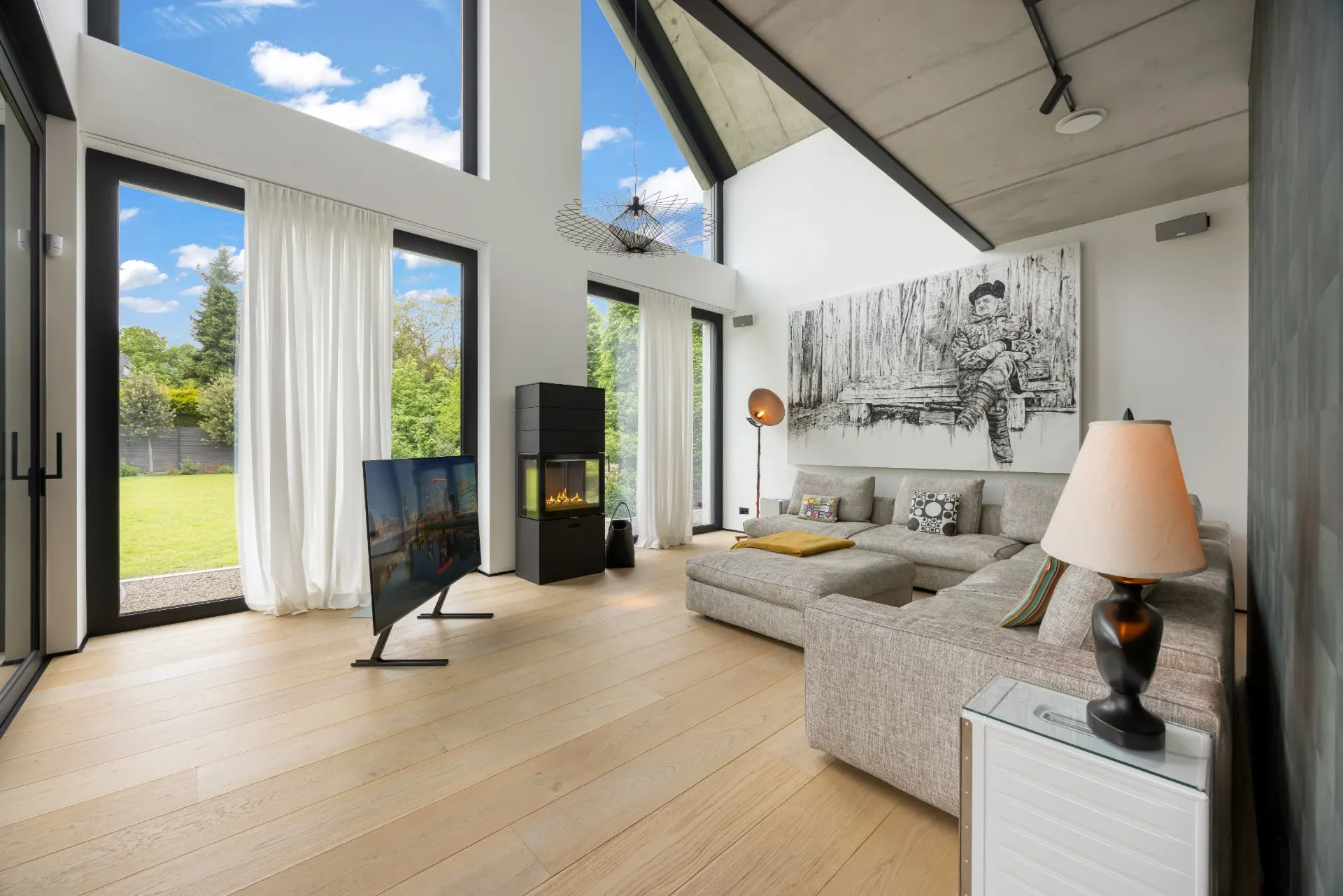 Modernes Wohnzimmer mit großer Fensterfront, hellen Vorhängen, Ecksofa und Kamin.