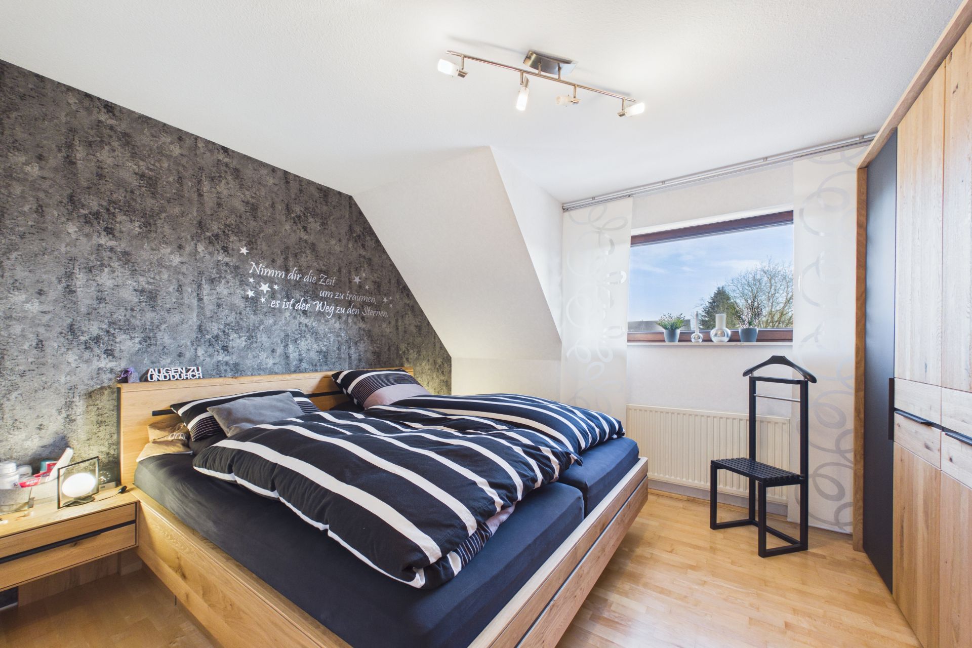Modernes Schlafzimmer mit Doppelbett, Nachttisch, Kleiderschrank und Fenster mit Blick nach draußen.