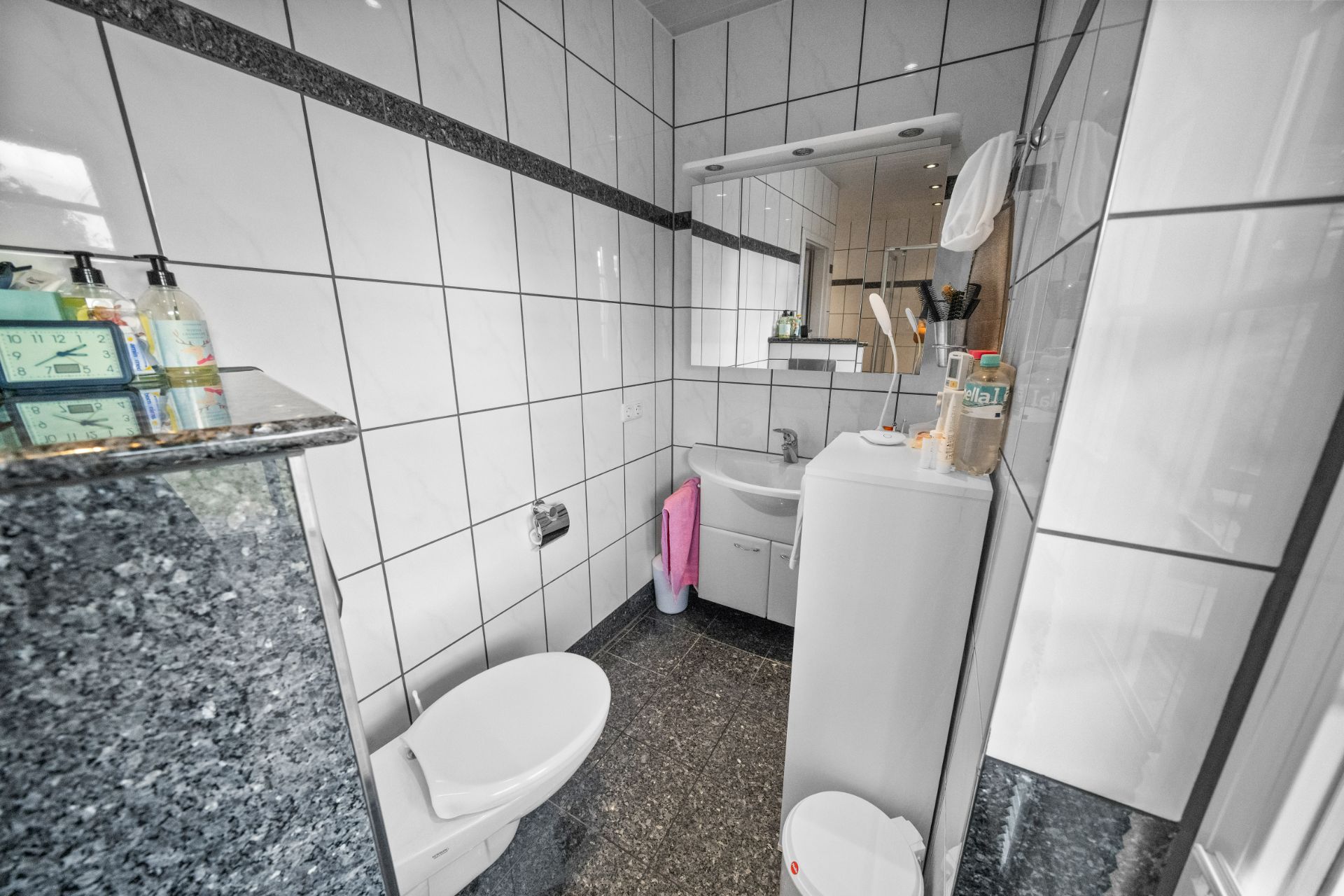 Kleines Badezimmer mit WC, Waschbecken, Spiegel und weißen Fliesen an Wand und Boden.