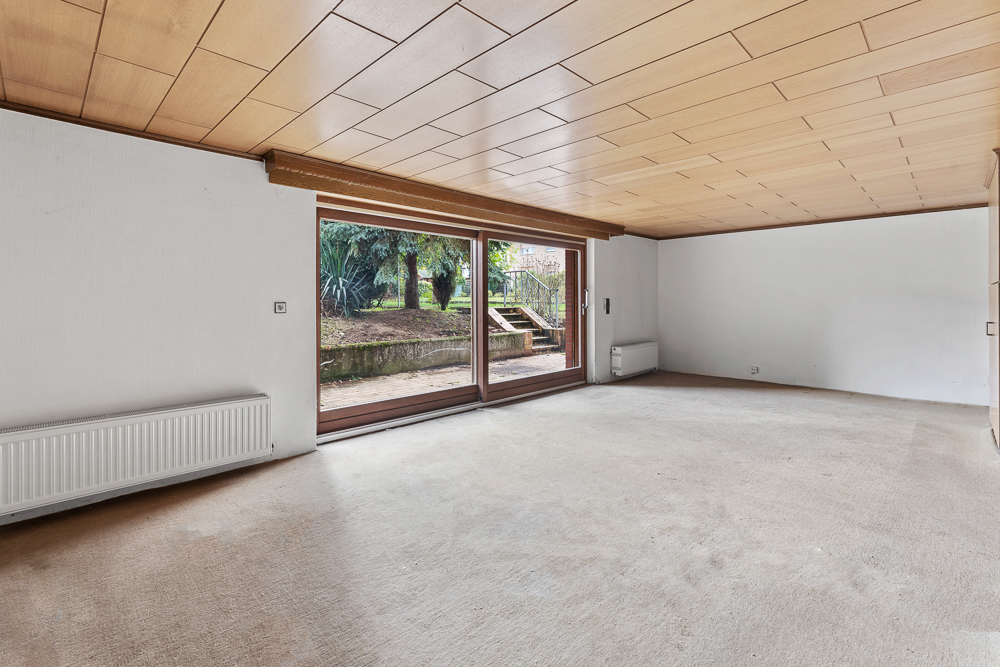 Leeres Zimmer mit Holzdecke und großen Fenstern mit Blick auf Garten.