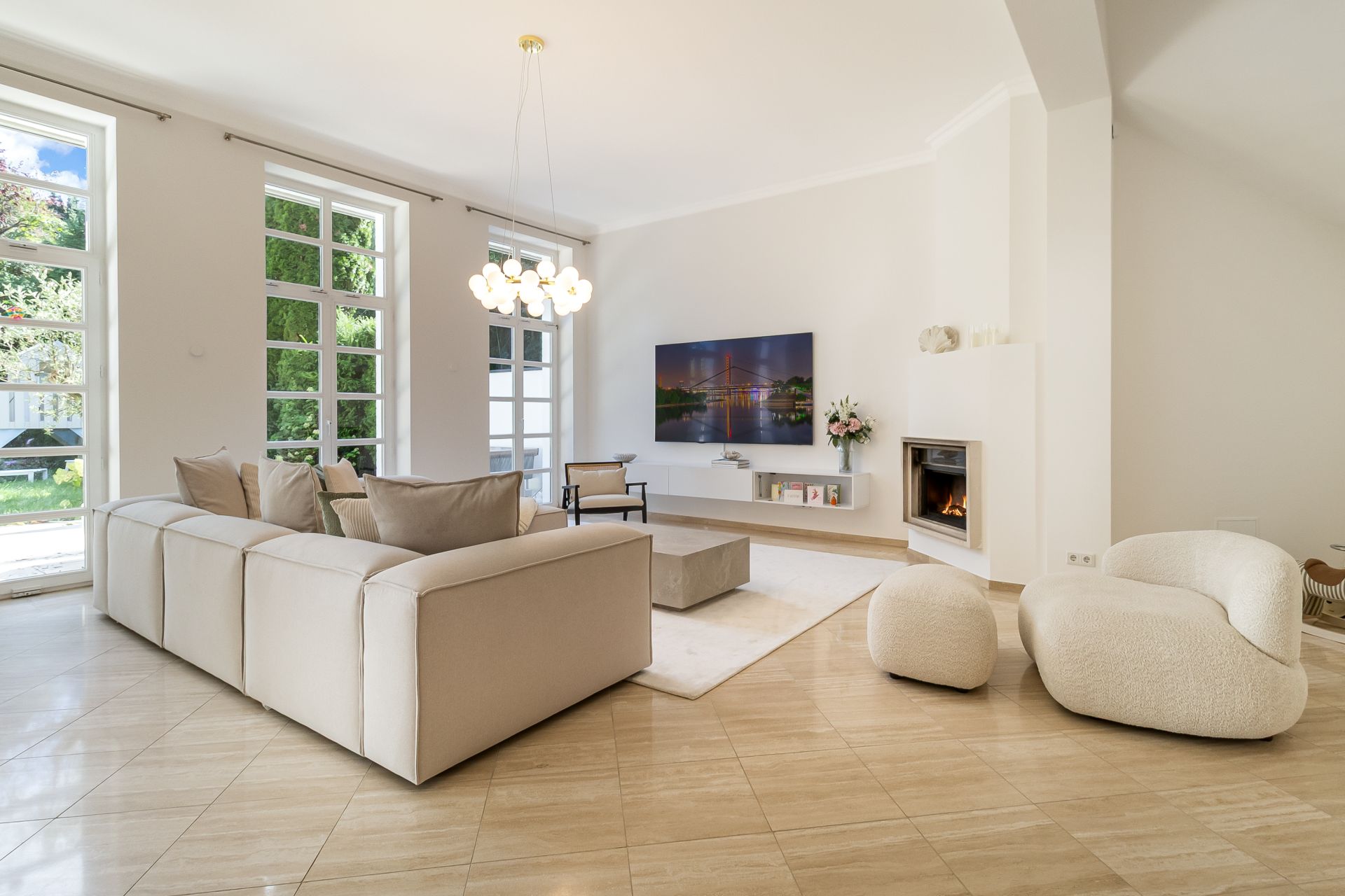 Helles Wohnzimmer mit beigen Möbeln, großem Sofa, Sessel, Fernseher und Kamin.