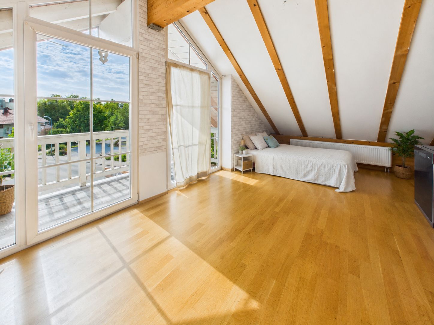 Helles Zimmer mit Holzboden, Einzelbett, großen Fenstern und Zugang zu einem Balkon.