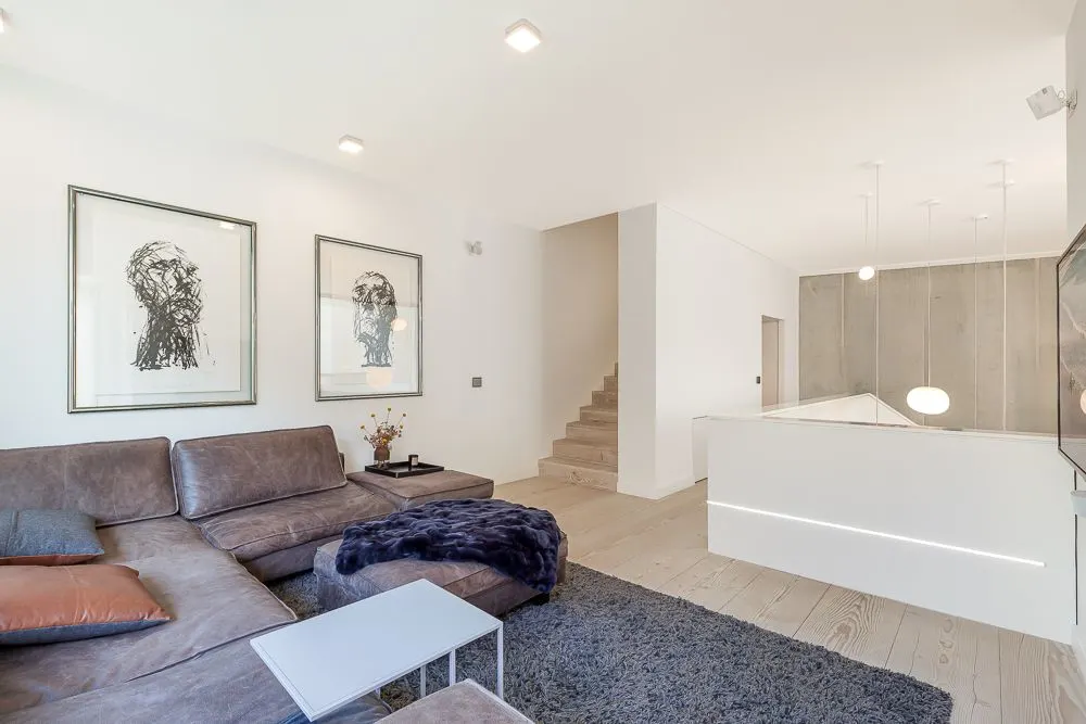 Modernes Wohnzimmer mit braunem Sofa, Teppich, zwei Bildern und offener Treppe.