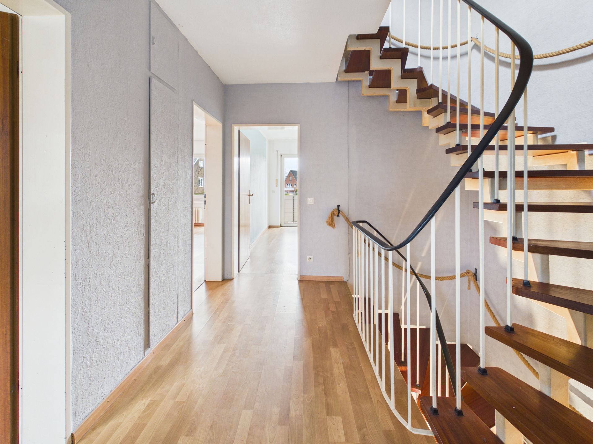 Heller Flur mit Holztreppe und Parkettboden in einem Wohnhaus.