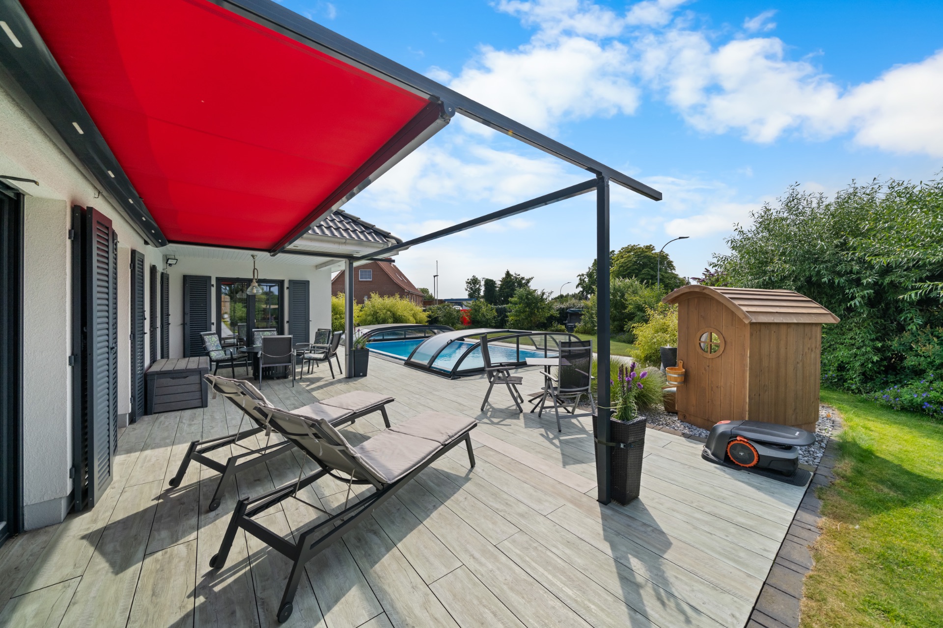 Große Terrasse mit roter Markise, Liegestühlen, Esstisch und überdachtem Pool im Garten.