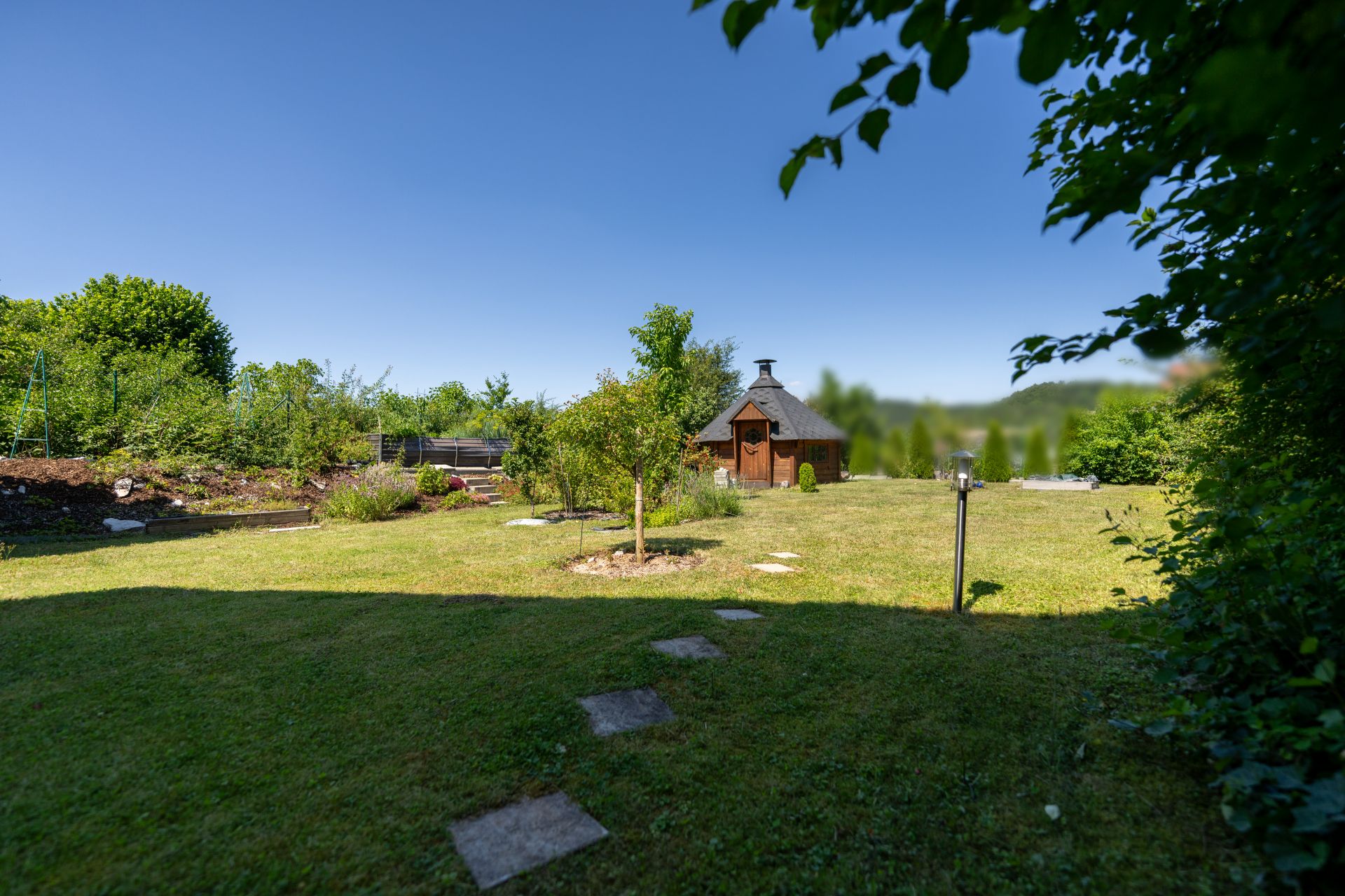 Garten mit Rasenfläche, Bäumen und einem kleinen Holzhaus im Hintergrund.