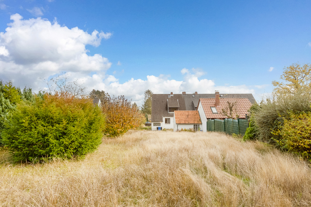 Blick auf ein Haus mit rotem Dach und großem, überwachsenem Garten im Vordergrund.