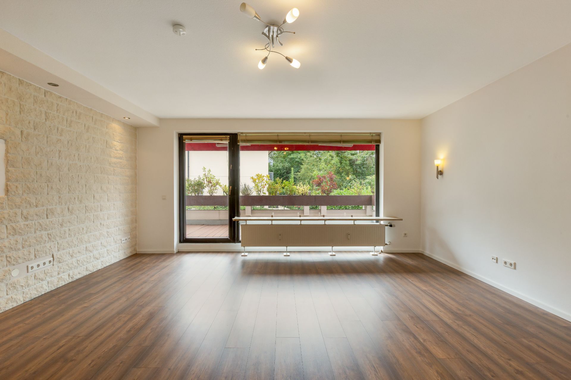 Helles Wohnzimmer mit Holzfußboden, Steinwand und großem Fenster zur Terrasse.