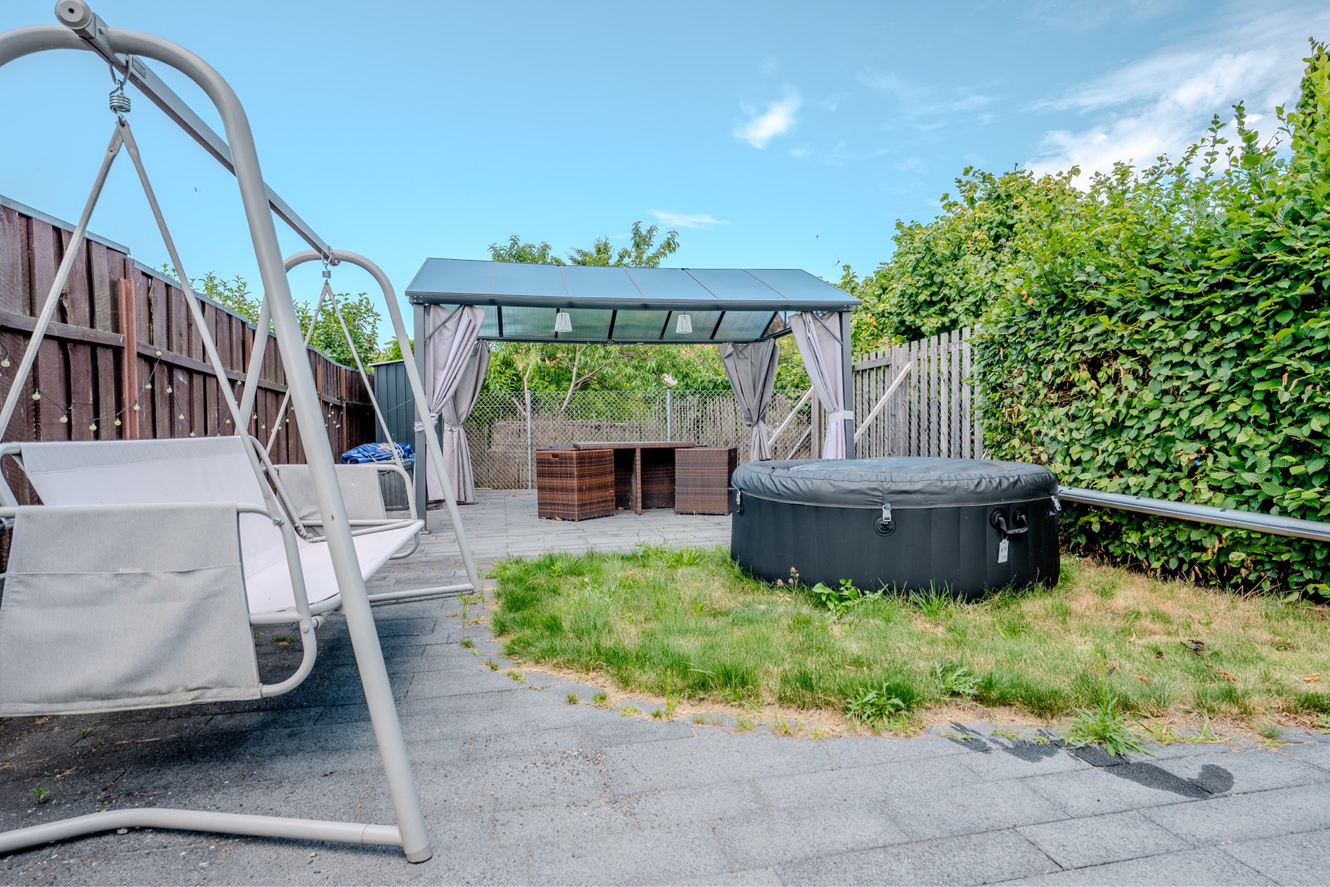 Gartenbereich mit Schaukelsitz, Pavillon, Gartentisch und rundem Whirlpool auf Rasen.