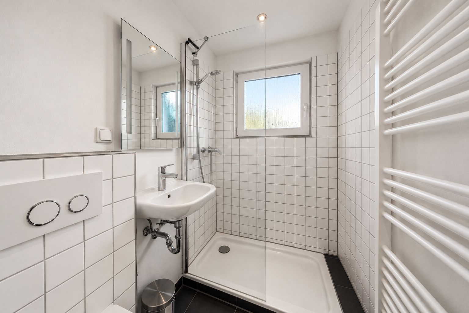 Modernes, kleines Badezimmer mit Dusche, Waschbecken und Fenster, weiße Fliesen an den Wänden.