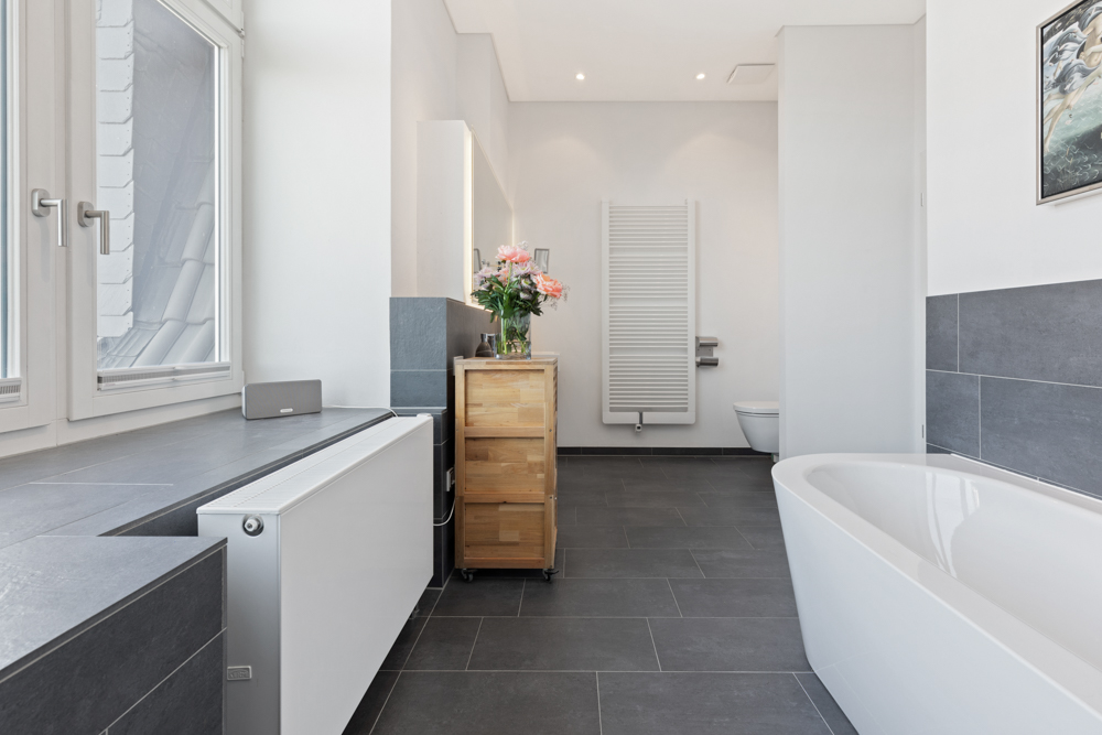 Modernes Badezimmer mit Badewanne, Holzmöbel, Fenster und Handtuchheizkörper.