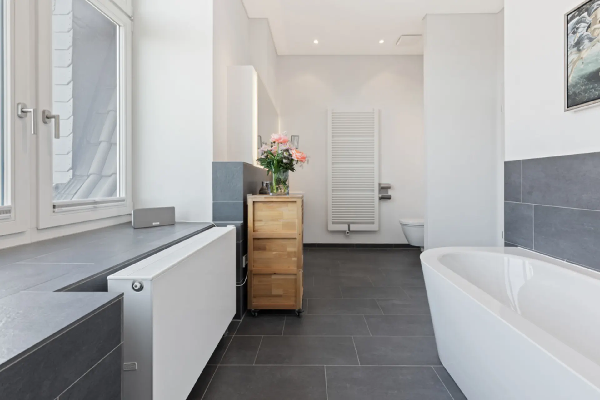 Modernes Badezimmer mit Badewanne, Holzmöbel, Fenster und Handtuchheizkörper.