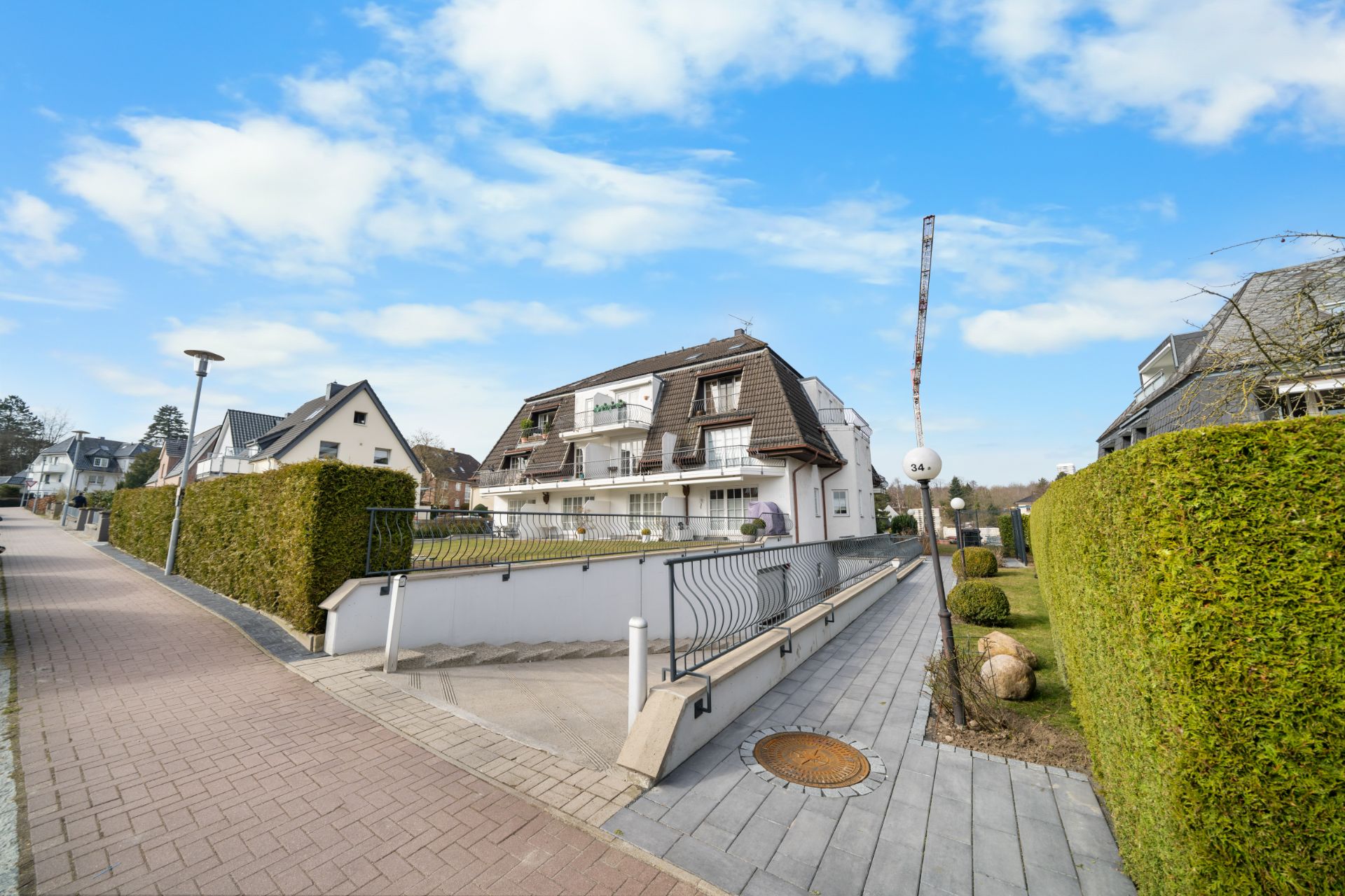 Mehrfamilienhaus mit Balkonen und Einfahrt zu einer Tiefgarage, daneben Gehweg und gepflegte Hecke.